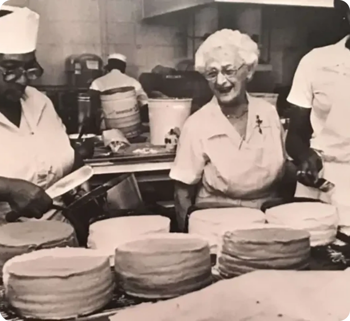Vintage black and white photo of Gambino’s Bakery staff preparing layered cakes in a New Orleans kitchen.